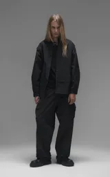 Chaqueta tipo overshirt de microfibra, color negro, con calce oversize y ruedo curvo. Presenta cierre frontal con broches a presión, bolsillos frontales de gran tamaño y cierres laterales a lo largo de las mangas para ajustar su amplitud.