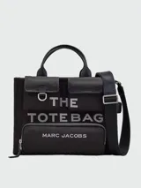 Cartera tote de lona color negro, modelo The Cargo Canvas Medium Tote Bag de Marc Jacobs. Presenta múltiples bolsillos frontales con solapa y cierre de cremallera, asas de mano superiores y una correa de hombro ajustable y extraíble. Cuenta con el nombre de la marca y la inscripción "THE TOTE BAG" estampados en el frente.