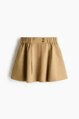 Pollera mini acampanada en sarga de algodón y lyocell, de cintura estándar con cierre, pretina prolongada con botones y elástico revestido en los lados. Cuenta con frunces en la parte superior y bolsillos laterales discretos.