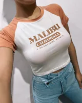 Remera corta blanca con mangas raglán de diferentes colores y estampado frontal con la leyenda "Malibu California A Beautiful Place".
