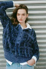 Jersey de punto con textura estructurada en tonos azules y negros, cuello polo con solapa, manga larga y cierre frontal parcial con botones.