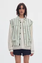 Chaleco oversize de denim color crudo con estampado de lunares negros, cuello camisero, bolsillos delanteros y cierre frontal de botones metálicos.