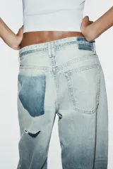 Jeans de tiro medio y corte baggy con cinco bolsillos, trabillas y rotos decorativos. Cuenta con detalle de cinturón confeccionado en el mismo tejido y cierre frontal con cremallera y botón metálico.
