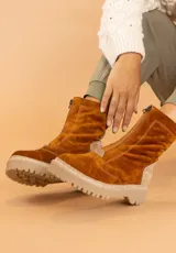 Bota tipo borcego de cuero color marrón oscuro con detalles en gamuza beige en el talón. Presenta cierre frontal, suela track de goma color beige con costuras visibles y forro interior de felpa.