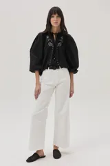 Blusa blanca con bordado floral en el cuello, mangas abullonadas 3/4 y cierre frontal con botones.