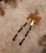 Aros colgantes marca Agnès, compuestos por una placa rectangular dorada en la parte superior y una cadena de piedras facetadas negras en la parte inferior.