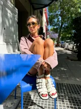 Sandalias planas de cuero color blanco hueso, con múltiples tiras horizontales y hebillas metálicas plateadas. Incluyen pulsera superior desmontable con hebillas laterales para regular el ajuste.