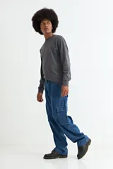 Pantalón tipo jean de corte baggy con diseño cargo, presenta bolsillos laterales amplios con solapa y costuras reforzadas. Confeccionado en denim de algodón con acabado lavado.