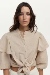Camisa de algodón a rayas color beige y blanco, con cuello mao, volados en los hombros, mangas abullonadas y nudo frontal en el dobladillo.