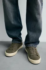 Zapatilla de cordones confeccionada en piel con acabado de serraje. Presenta un diseño liso con detalle de color a contraste en el talón y suela plana de goma a contraste.