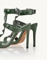 Sandalias de tacón alto color verde oliva, con punta cuadrada, tiras con tachas piramidales y pulsera al tobillo con hebilla.