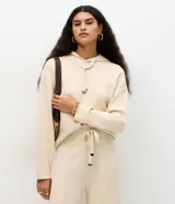 Buzo de punto color beige con capucha y cordones largos con punteras metálicas, de corte regular y mangas largas.