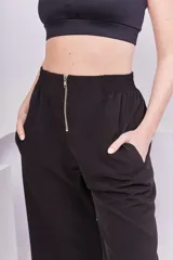 Pantalón negro de corte recto y tiro alto, con cintura elástica, bolsillos laterales y cierre metálico frontal.