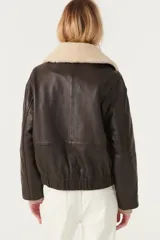 Chaqueta corta de cuero color marrón con cuello de piel sintética color crema, cierre con botones a presión, bolsillos frontales con solapa y puños con botón.