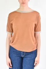 Remera de tejido de punto color terracota, con escote barco y mangas cortas. El cuello y los puños tienen un ribete en color beige claro con hilo metálico.