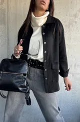 Chaqueta de gamuza negra con cierre frontal de botones metálicos, bolsillos laterales y cuello camisero.