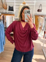 Blusa de color bordó con cuello drapeado y detalle de cinta tipo choker integrada. Presenta mangas largas con puños abotonados y un corte holgado y fluido.