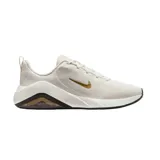 Championes Nike Bella 7 color blanco con logo dorado, diseñados para entrenamiento, con capellada de malla elástica y transpirable, tecnología Air Zoom en el talón, entresuela de espuma suave y suela de goma.