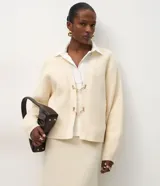 Cardigan de punto color crema con calce oversize, mangas amplias y cierre frontal mediante hebillas metálicas decorativas. Presenta una textura estructurada y puños ajustados.