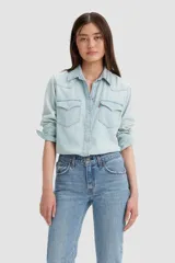 Camisa de denim celeste claro, de corte clásico, con cierre de botones a presión, mangas largas con puños abotonados, cuello americano y dos bolsillos frontales con solapa abotonada.