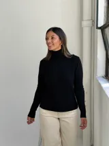 Polera negra de cuello alto y manga larga, con detalle de botones dorados en los puños. Diseño ajustado al cuerpo con tejido de punto fino.