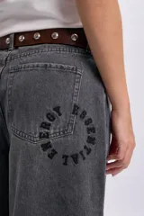 Pantalón jean ancho color gris claro, de corte holgado y tiro medio con estampa circular en el bolsillo trasero.