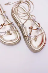 Sandalias negras de ecocuero con plataforma plana y tiras finas que se atan alrededor del tobillo.