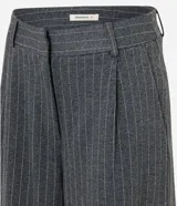 Pantalón de corte amplio tipo pantalona, confeccionado en tejido con patrón de rayas diplomáticas. Presenta cintura alta con trabillas para cinturón y cierre frontal tradicional.