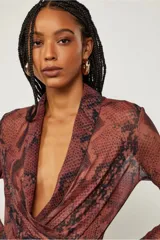 Body de poliéster y elastano con estampado de piel de serpiente en tonos marrones y negros. Tiene mangas largas, escote en V cruzado y calce ajustado al cuerpo.