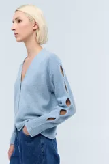 Cárdigan corto celeste de lana con lentejuelas, escote en V, cierre frontal con botones y mangas largas con aberturas.