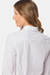 Camisa blanca de corte entallado, manga larga con puños abotonados y cuello clásico. Presenta cierre frontal con botones ocultos bajo una tapeta.