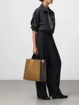 Bolso shopper de estructura cuadrada en color marrón con acabado brillante y textura craquelada. Cuenta con asas de mano y asa larga para hombro en color negro, cierre de solapa interior con cremallera y bolsillo interior. Logo grabado en la parte frontal.