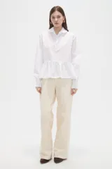 Camisa blanca de corte peplum con cuello tipo polo con volados, cierre frontal de botones y mangas largas con puños ajustados.