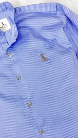 Camisa celeste con rayas verticales blancas, cuello mao y mangas largas con puños abotonados.