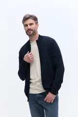 Campera de tejido de punto liviano color beige, con cierre frontal completo y cuello alto tipo bomber. Presenta un pequeño logo bordado en el pecho y puños acanalados.