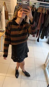 Sweater de tejido de punto con diseño de rayas horizontales en tonos marrón y negro, con acabado brillante. Presenta cuello polo con cierre frontal de botones y mangas largas con puños acanalados.