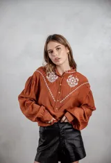Camisa de manga larga color terracota con detalles bordados en hilo blanco en la parte frontal y hombros, escote en V y cierre frontal de botones.