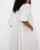 Vestido camisero midi blanco de algodón orgánico, con cuello tipo tira, mangas raglán sobre el codo, botonadura frontal oculta y canesú con pliegues en la espalda.