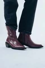 Bota de caña media confeccionada en cuero negro con acabado brillante, diseño de silueta limpia, puntera cuadrada y taco cuadrado de altura media.