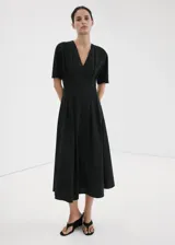 Vestido midi de corte evasé color negro, con diseño largo, cuello en pico, detalles fruncidos y manga corta. Cuenta con cierre de cremallera en la parte posterior.