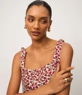 Blusa de viscosa y lino con estampado floral en tonos rojos y blancos. Presenta escote cuadrado, cuerpo ajustado con fruncido en la cintura y bajo con volado (peplum). Los breteles son anchos y se atan con lazos en los hombros.