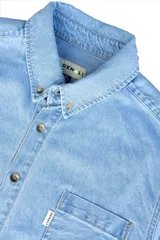 Camisa de jean celeste, de corte clásico, con cuello abotonado, manga larga y bolsillo en el pecho.
