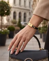 Pulsera de diseño profesional con placa central rectangular de acero dorado que presenta un grabado de tijeras. La estructura combina la placa con segmentos de cuerina negra y detalles metálicos, ofreciendo un estilo moderno y temático.