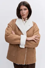 Cazadora de efecto piel en color tostado con interior y solapas de borreguillo blanco. Presenta cierre frontal con botones, bolsillos laterales y mangas largas con puños de borreguillo.