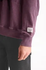 Hoodie y canguro oversize violeta con efecto acid wash, capucha y bolsillo frontal tipo canguro. Presenta un pequeño estampado tipográfico en el pecho con la inscripción 'DAUNTLESS // GOODS & SUCCESS CO'.