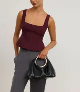 Cartera de mano Satinato tipo clutch, confeccionada en poliuretano color negro. Presenta un diseño moderno con una asa rígida metálica en formato ovalado y cuerpo estructurado.