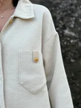 Camisa color crema tejida en lana, con cuello clásico, cierre frontal con botones dorados, dos bolsillos con solapa en el pecho y mangas largas con puños abotonados.