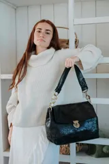 Cartera de hombro confeccionada en cuero con acabado texturizado, cuenta con una solapa frontal con cierre de broche metálico y una cadena decorativa en los laterales de la correa.