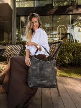 Cartera bandolera de gran tamaño en símil cuero color marrón con efecto desgastado. Cuenta con asa corta fija, correa larga regulable y placa metálica con logo en la parte frontal.
