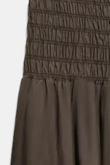 Mono largo de escote recto y hombros descubiertos, con cuerpo superior elástico tipo nido de abeja. Presenta piernas holgadas con bajo acabado en puño elástico ajustable mediante cordones.